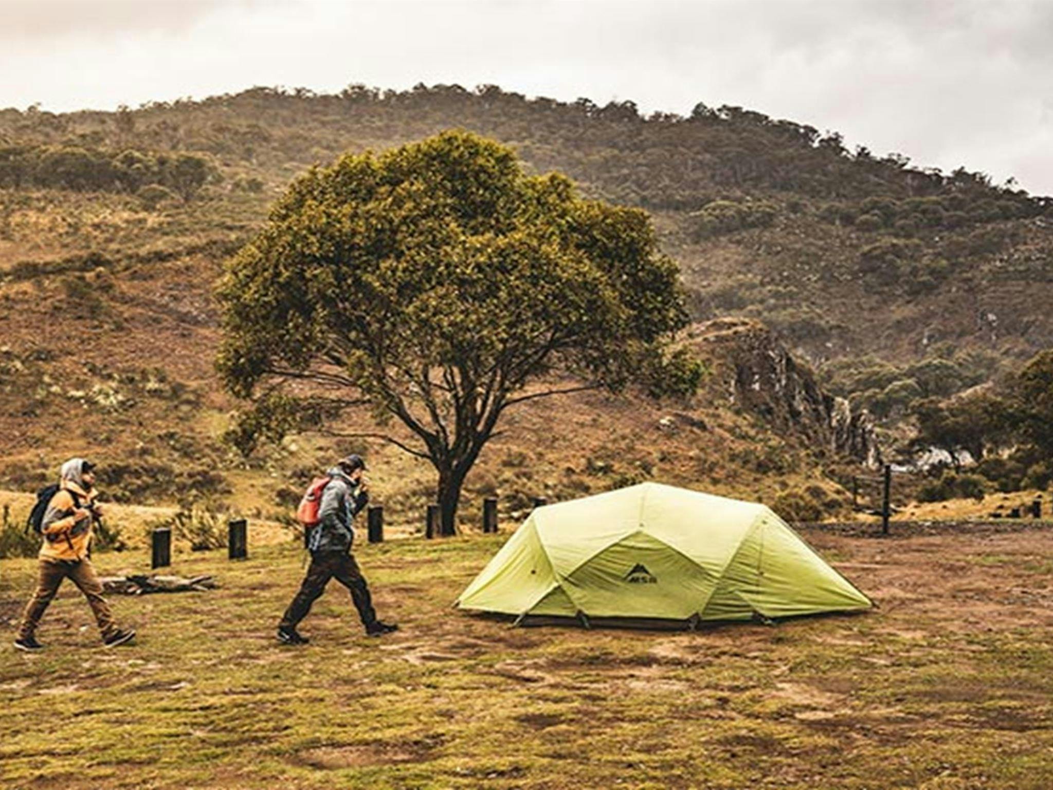 Two men walk past a green tent at Blue Waterholes campground, Kosciuszko National Park. Photo:
