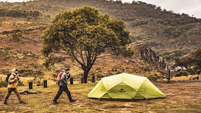 Two men walk past a green tent at Blue Waterholes campground, Kosciuszko National Park. Photo: