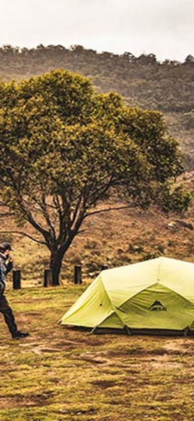 Two men walk past a green tent at Blue Waterholes campground, Kosciuszko National Park. Photo: