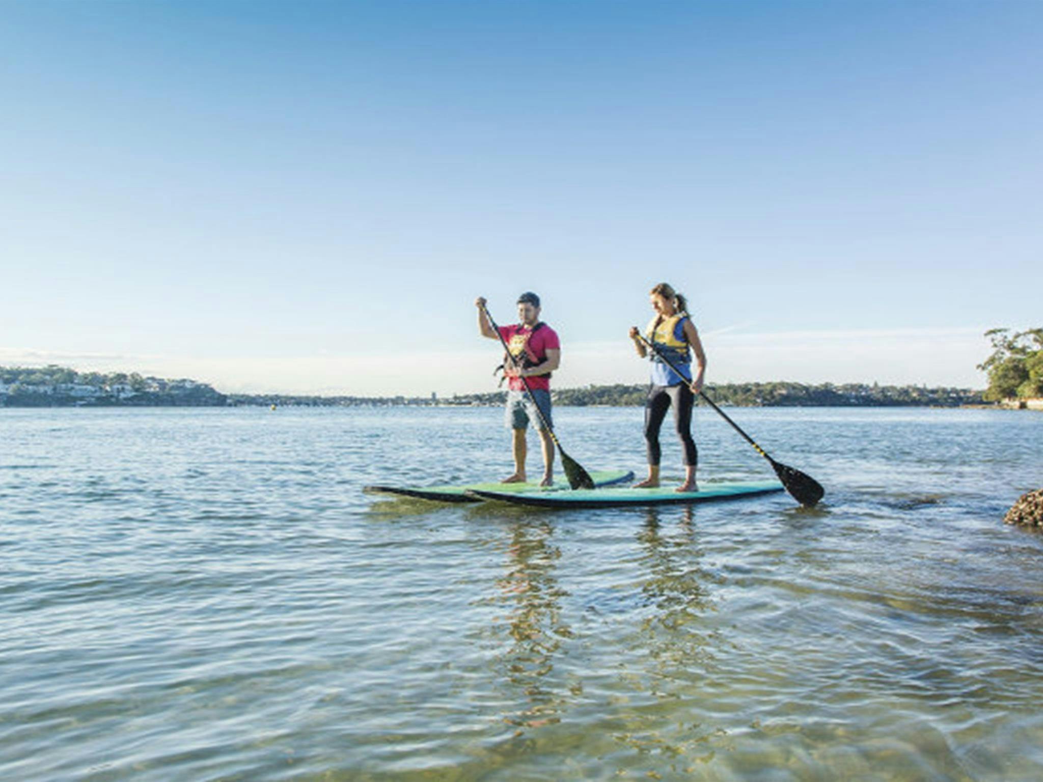 Two people stand-up paddle boarding in Cabbage Tree Basin, next to Bonnie Vale picnic area in Royal