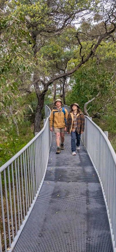 A man and a woman walking on a narrow steel track to Adams lookout and picnic area, Bungonia