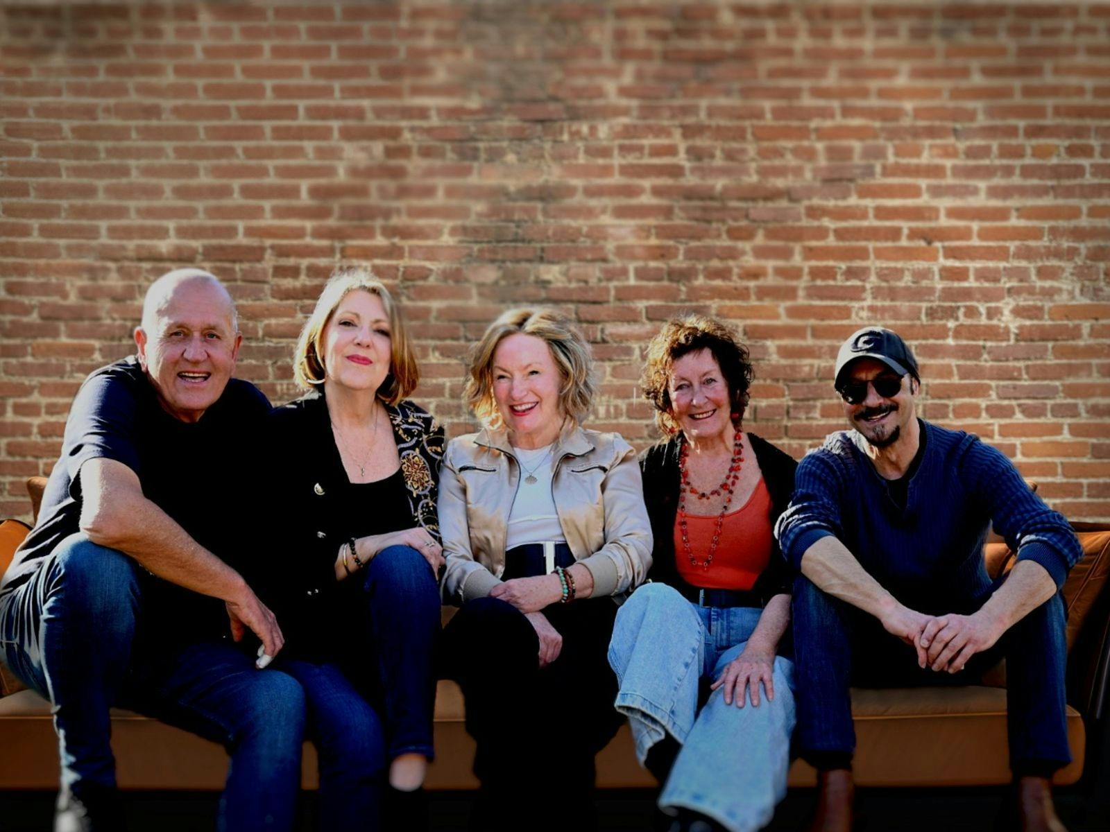 Five people sitting on a large couch with a brick wall in the background