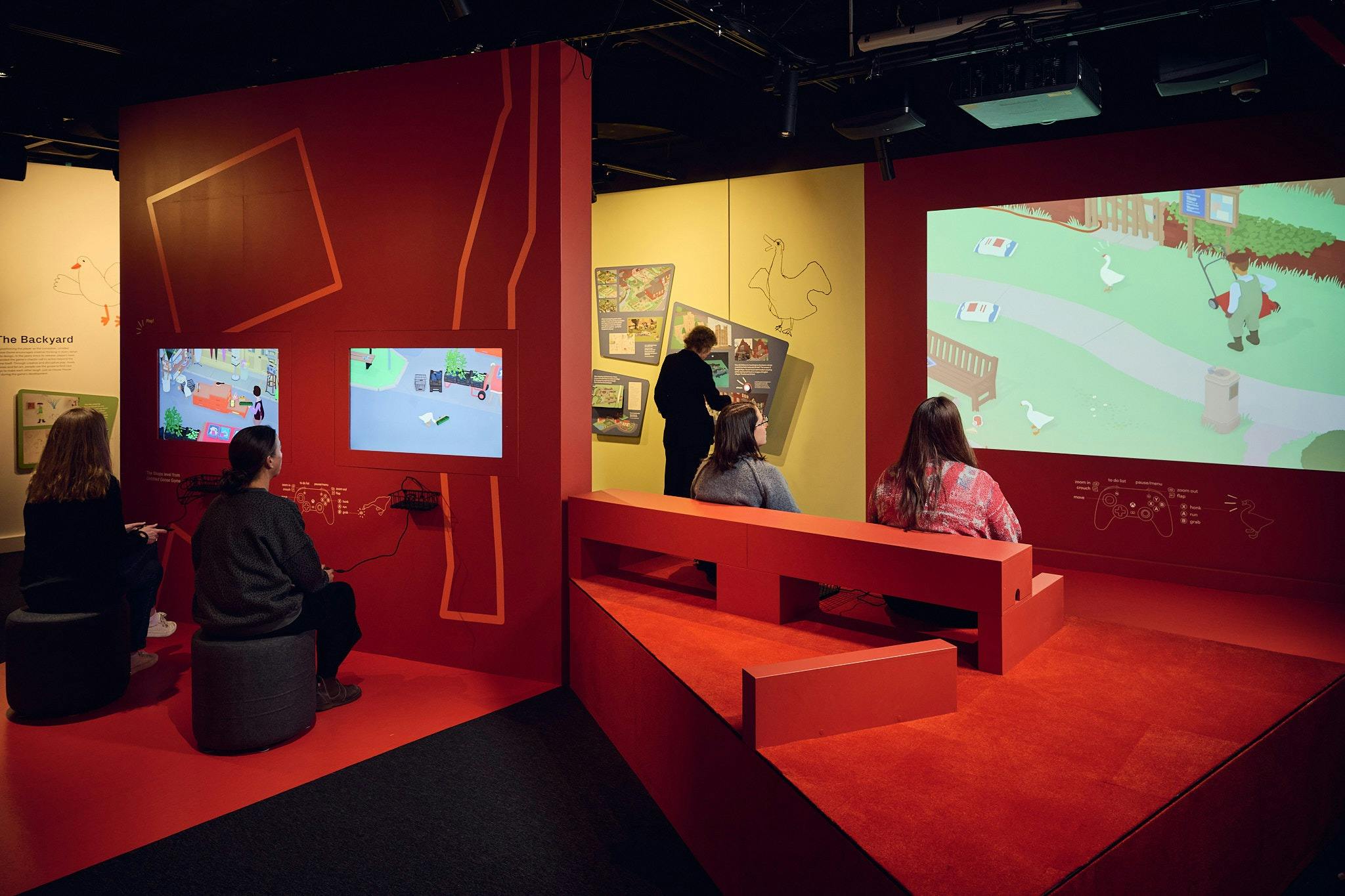 Exhibition space with red and yellow walls featuring multimedia displays and interactives