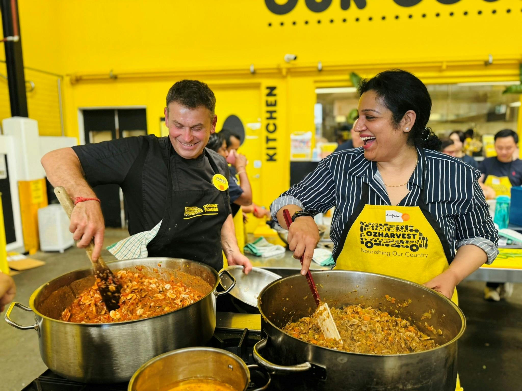 Two people cooking together at an OzHarvest Cooking for a Cause Social class, stirring large pots of