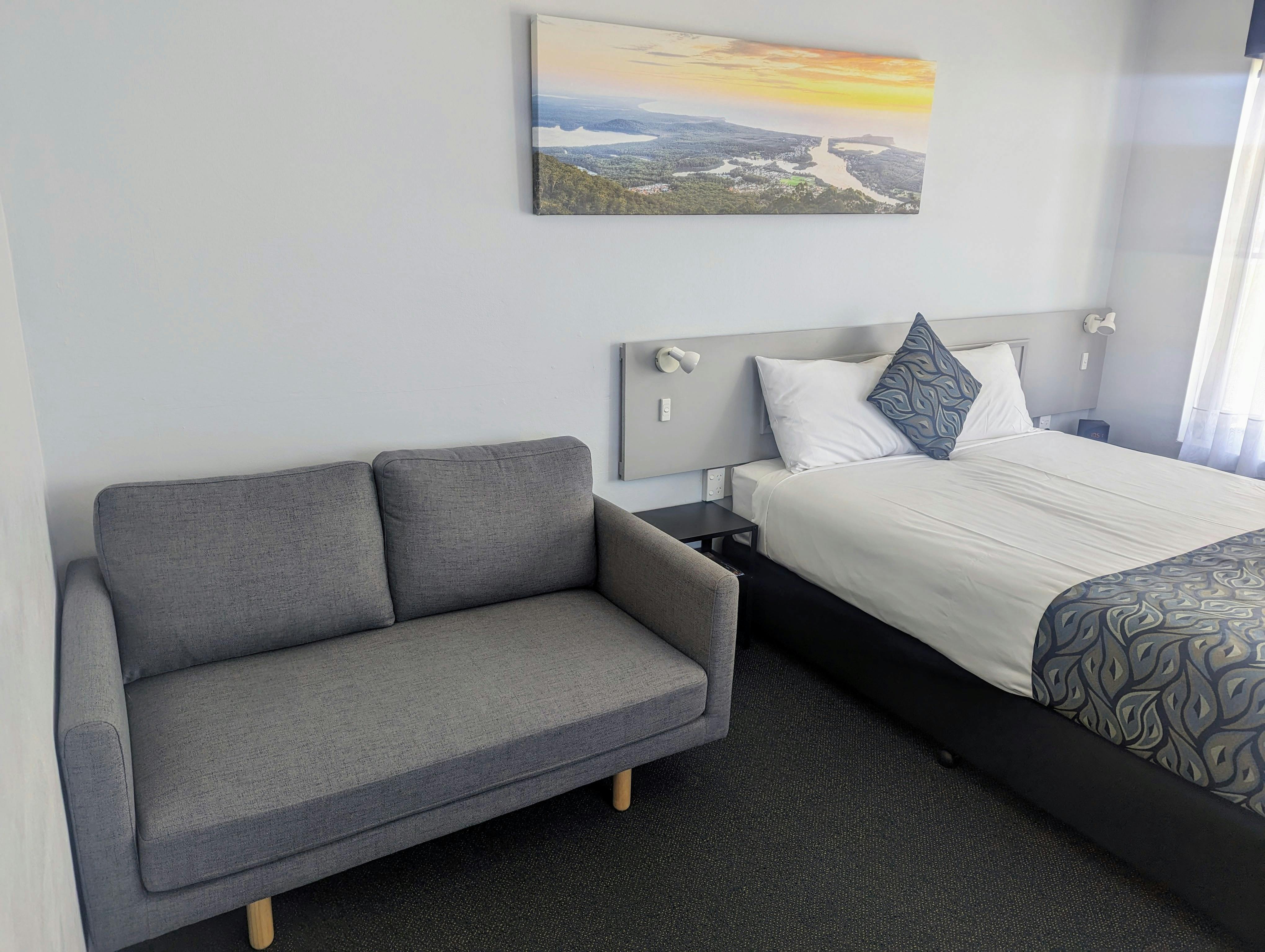 Queen motel room showing queen bed and 2 seater grey sofa.