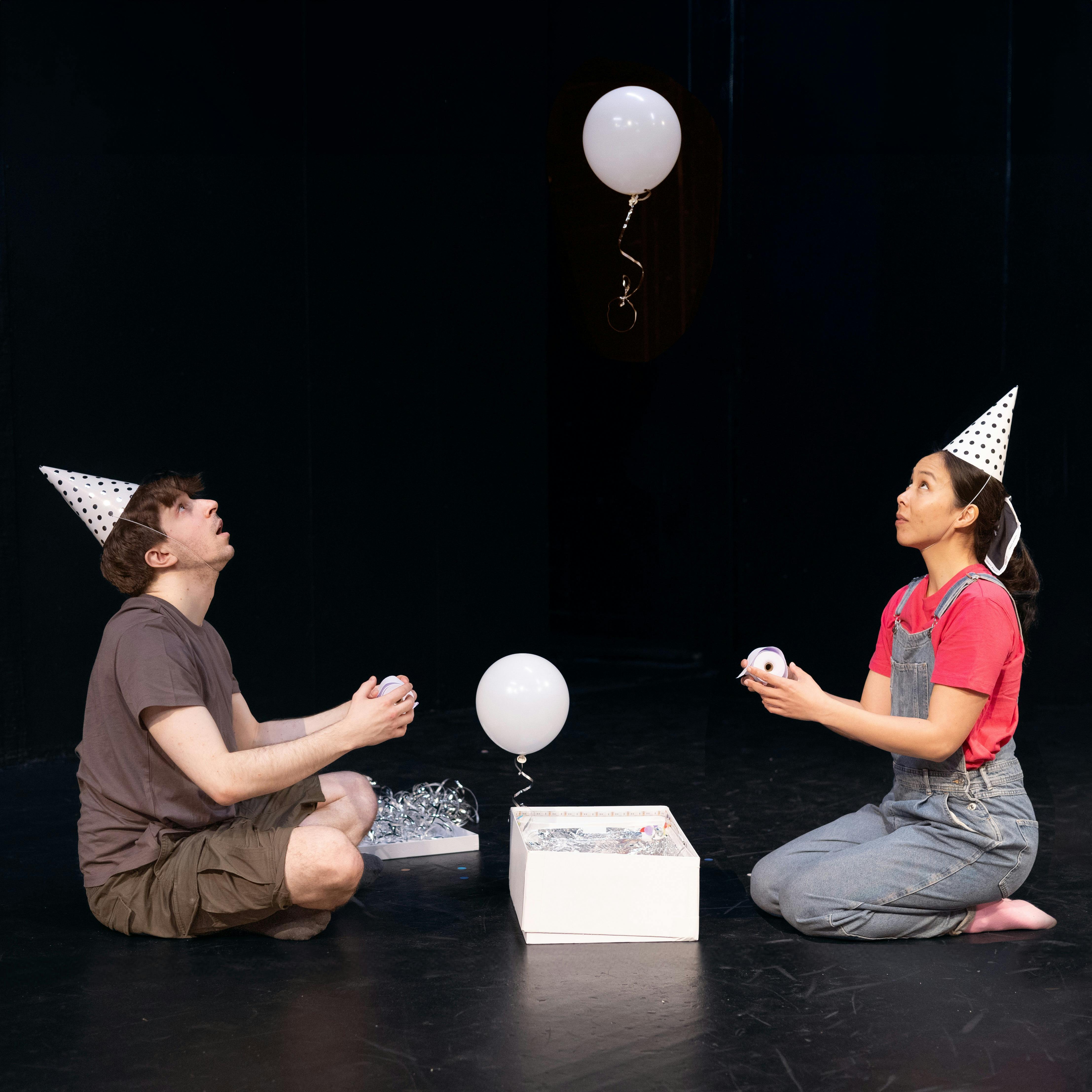 Man and woman with birthday hats watching a balloon float  out of a gift box