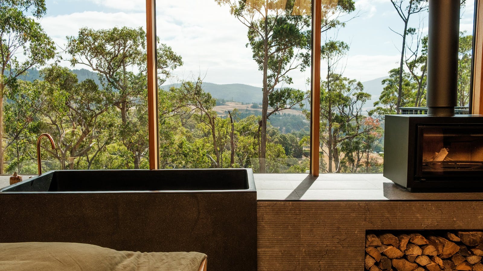Image of the view over the Huon Valley next to the deep stone composite tub, and fireplace at Hunter