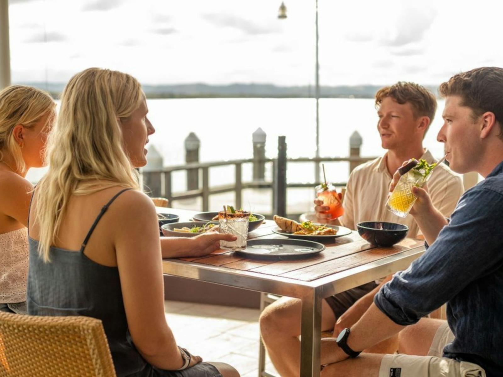 4 young people sitting around a table near the river having drinks