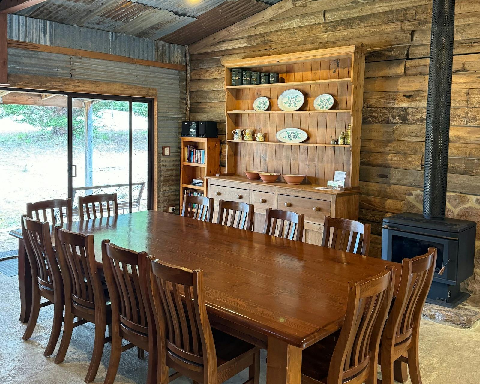 Large timber dining table with chairs in front of a timber buffet and wood heater
