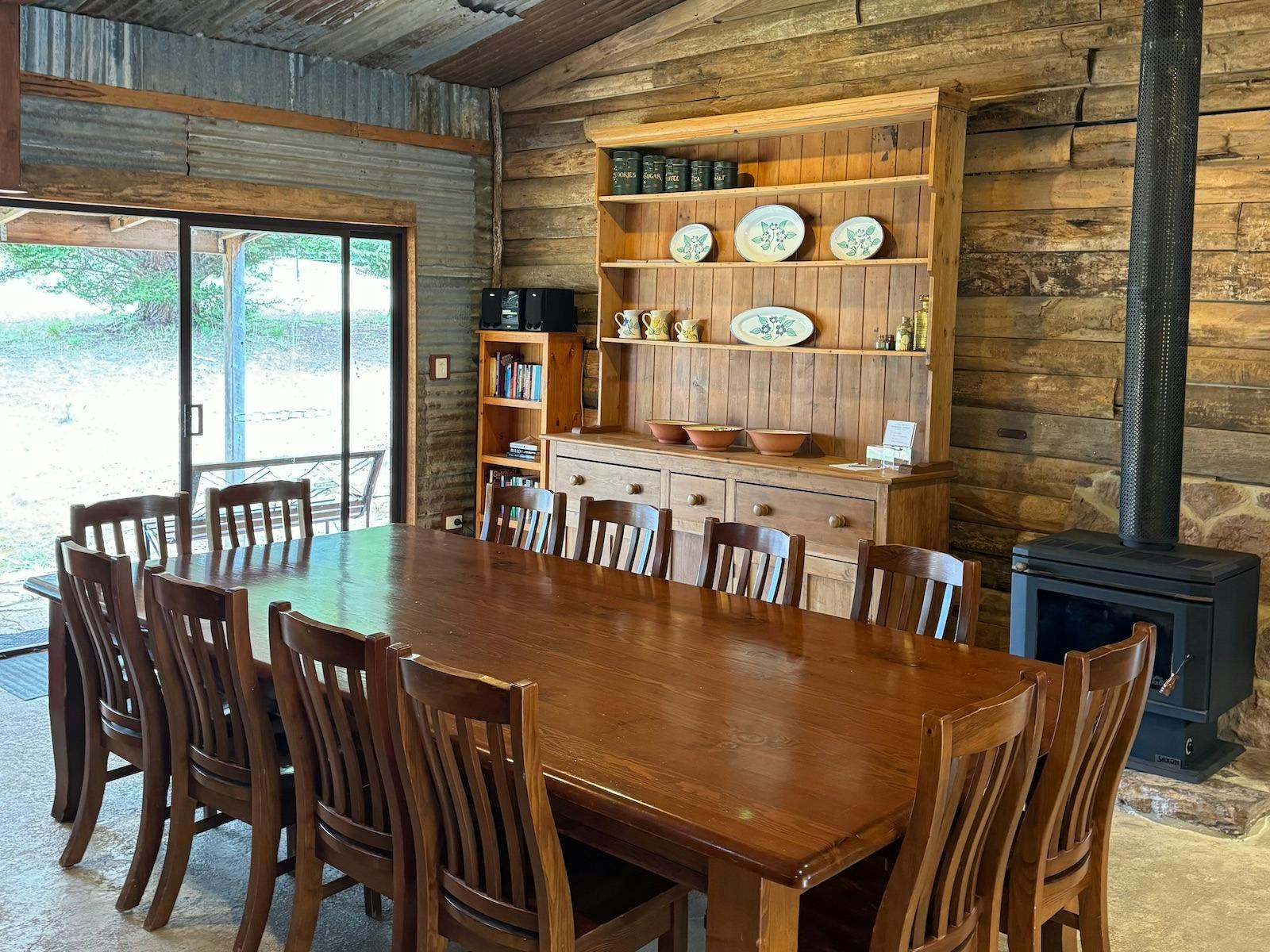 Large timber dining table with chairs in front of a timber buffet and wood heater
