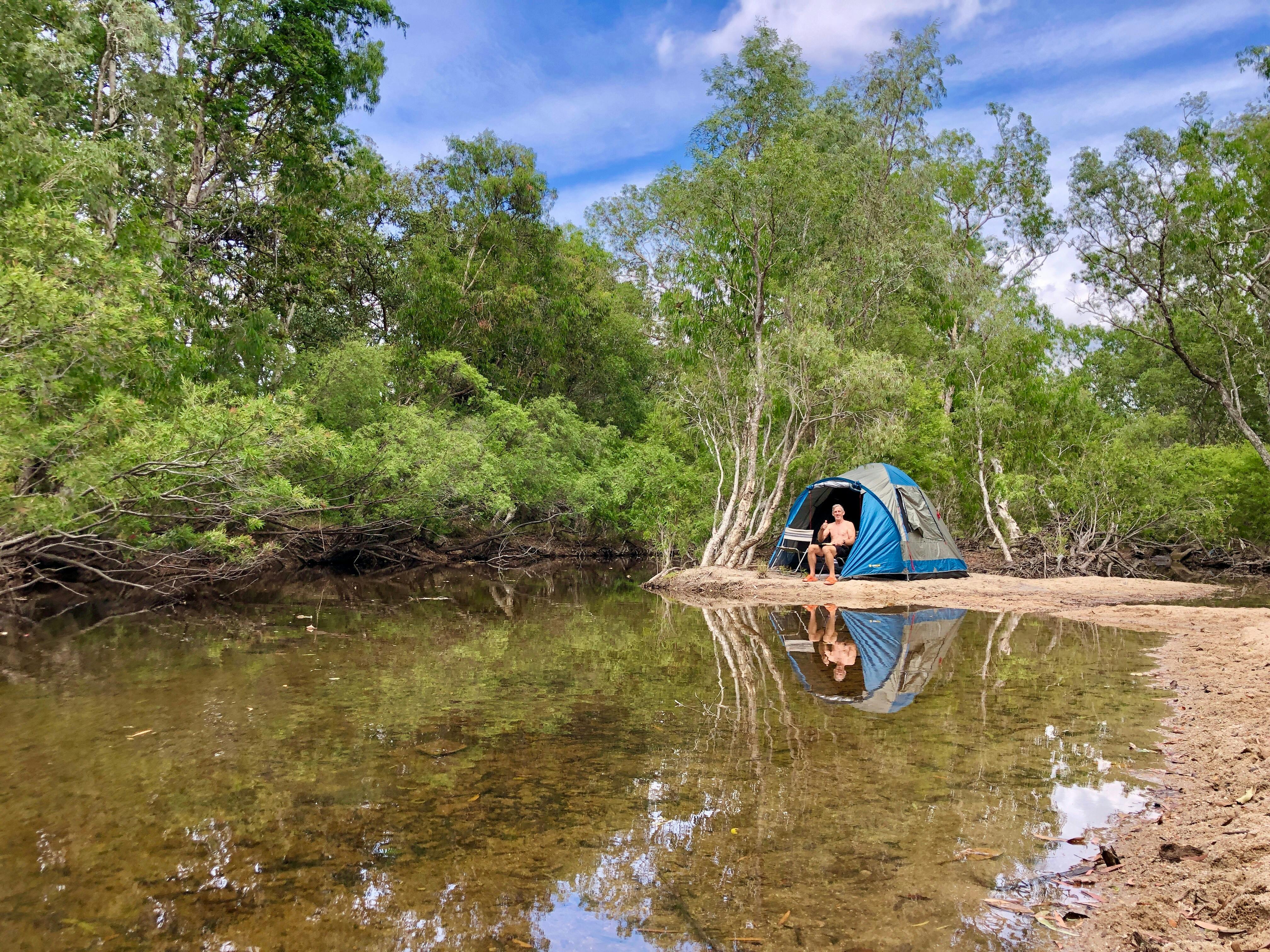 man sitting by tent next to creek