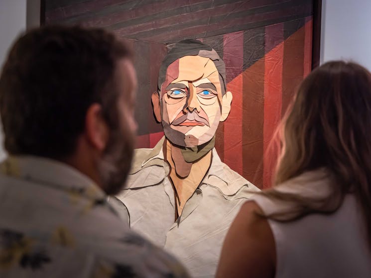 Two people look at a portrait of a man.