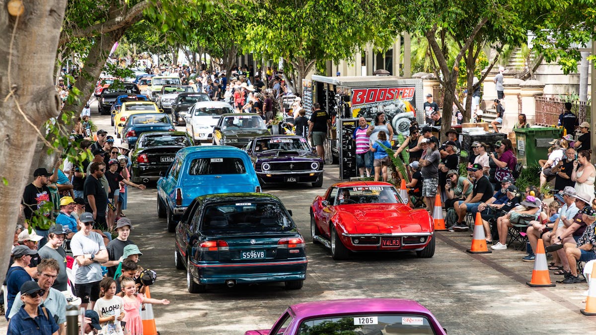 Classic and custom cars driving past crowds on a city street during Rockynats.