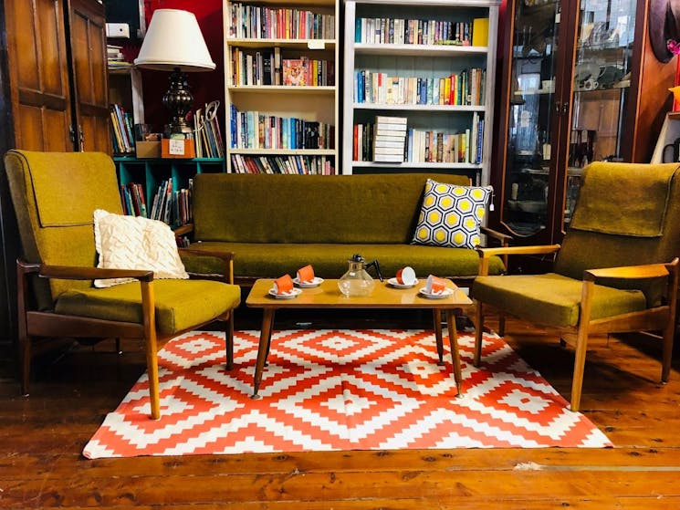 Two vintage green seats and 1 green couch sitting in front of a bookshelf and on a red and white rug