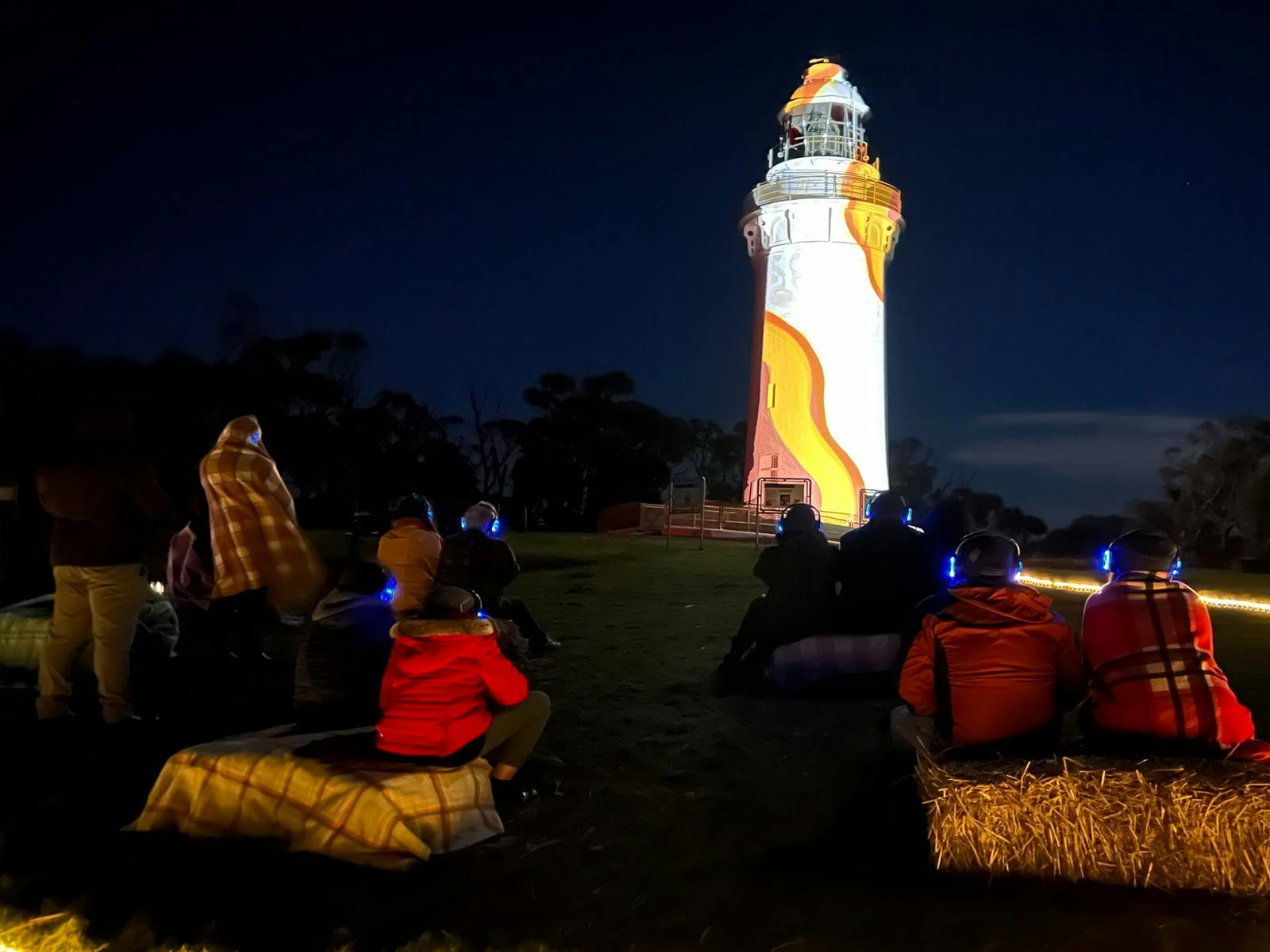 People sitting on hay bales watching projected images onto Table Cape lighthouse in Wynyard.
