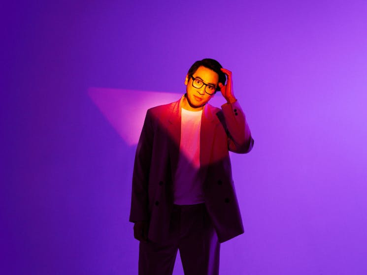 A person in a stylish suit and glasses stands against a vibrant purple background.