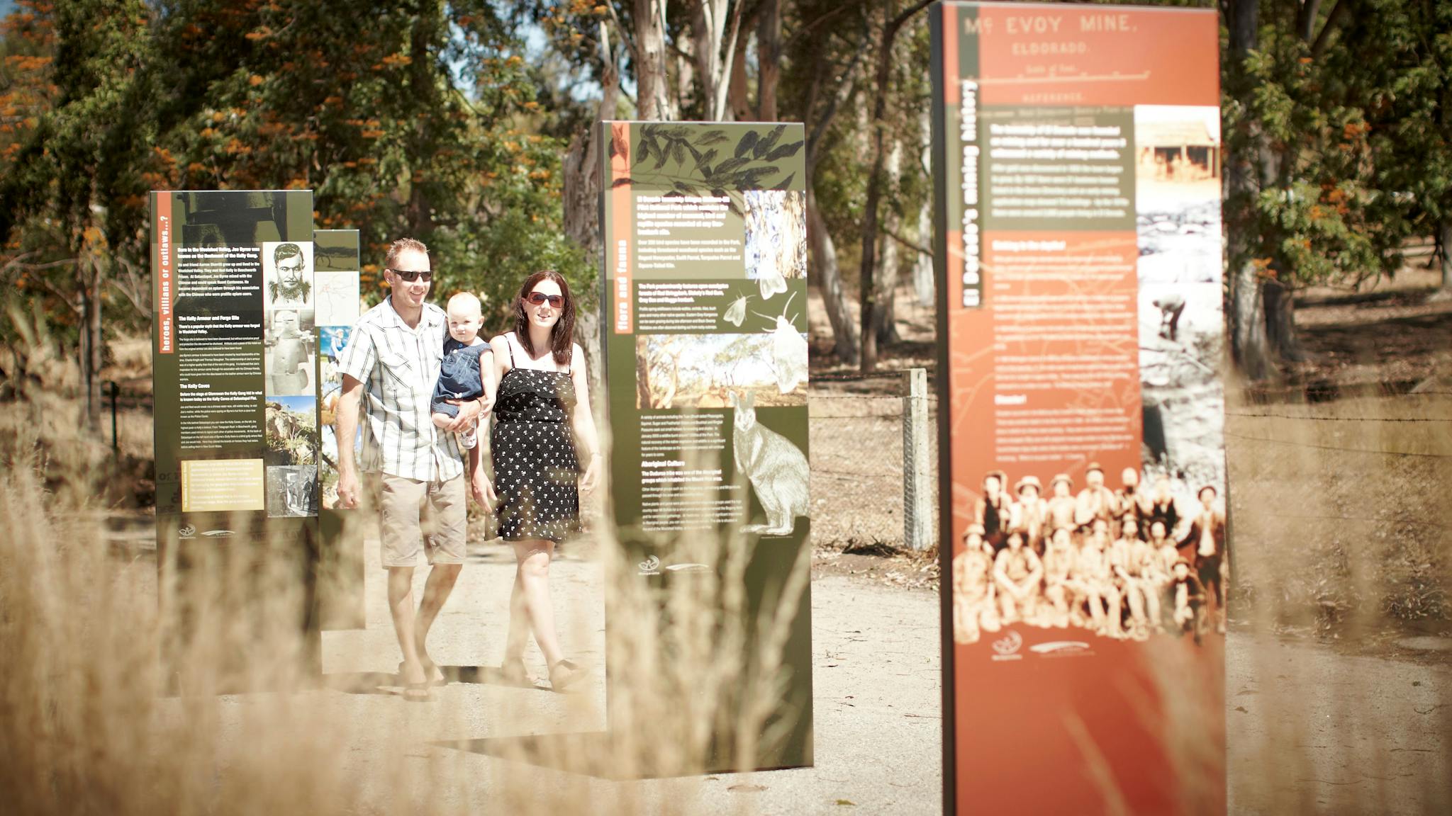 Family walking along path in the sun, looking at interpretive signage