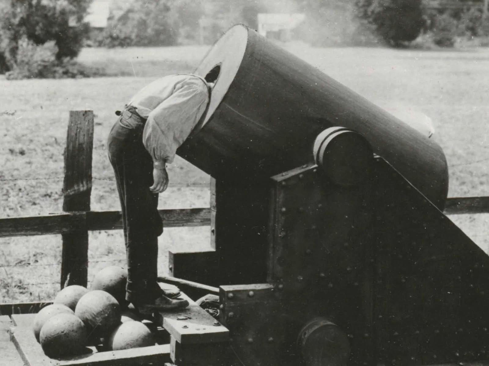 Buster Keaton looks directly out from inside the dark barrel of a massive railway cannon.