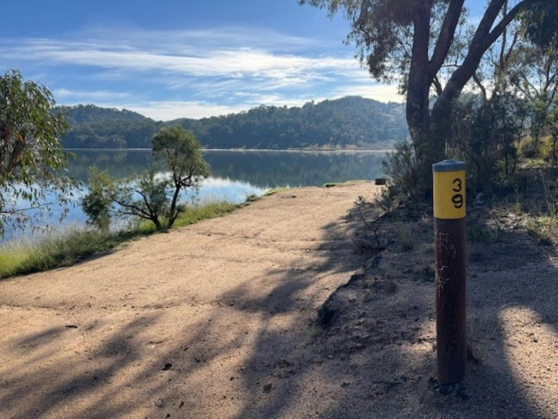 A bollard with yellow marker black number 39 stands in front of an open campsite and the lake behind