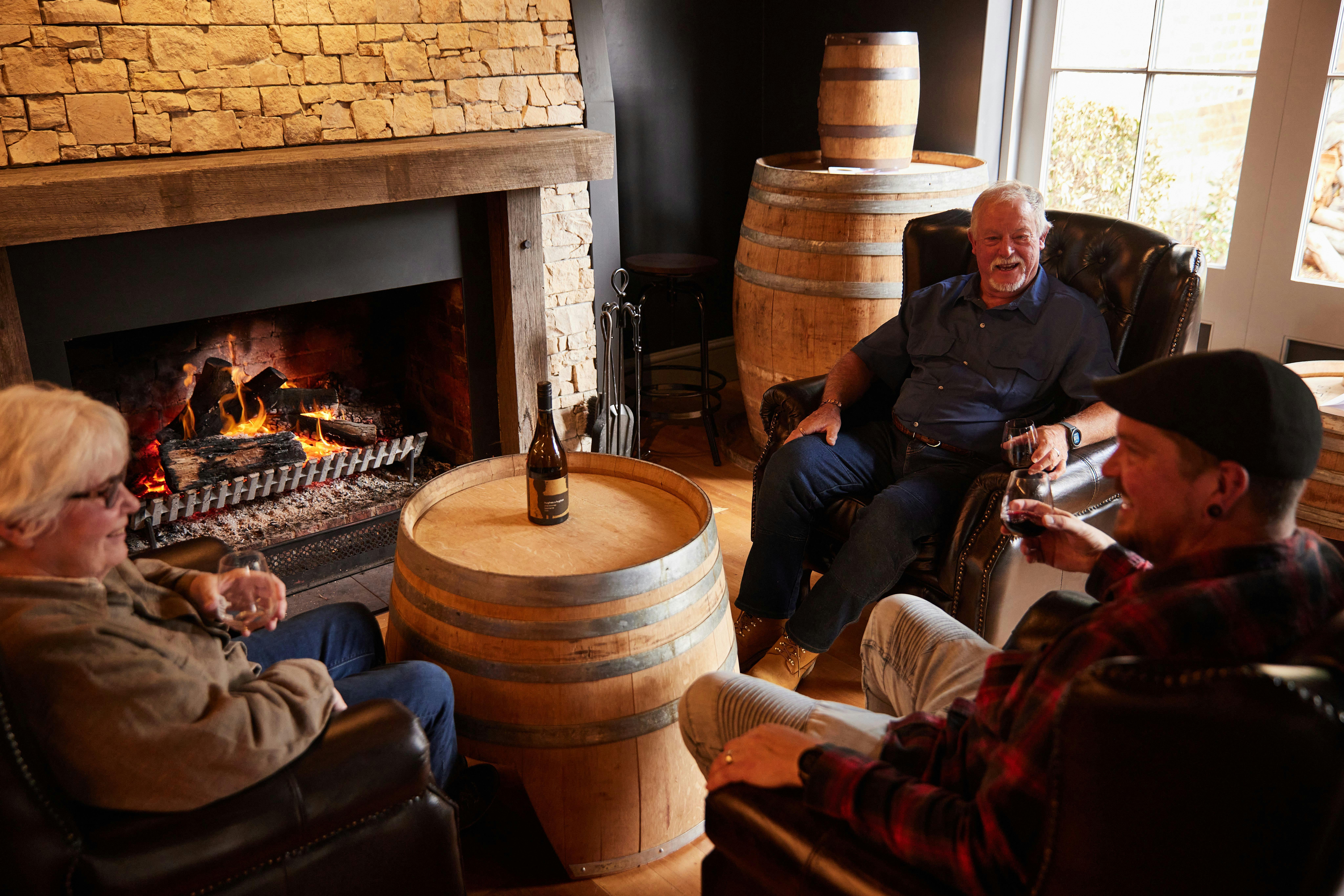 Three guests enjoying a drink in front of the  warm fireplace at Drink Tasmania Tasting House.