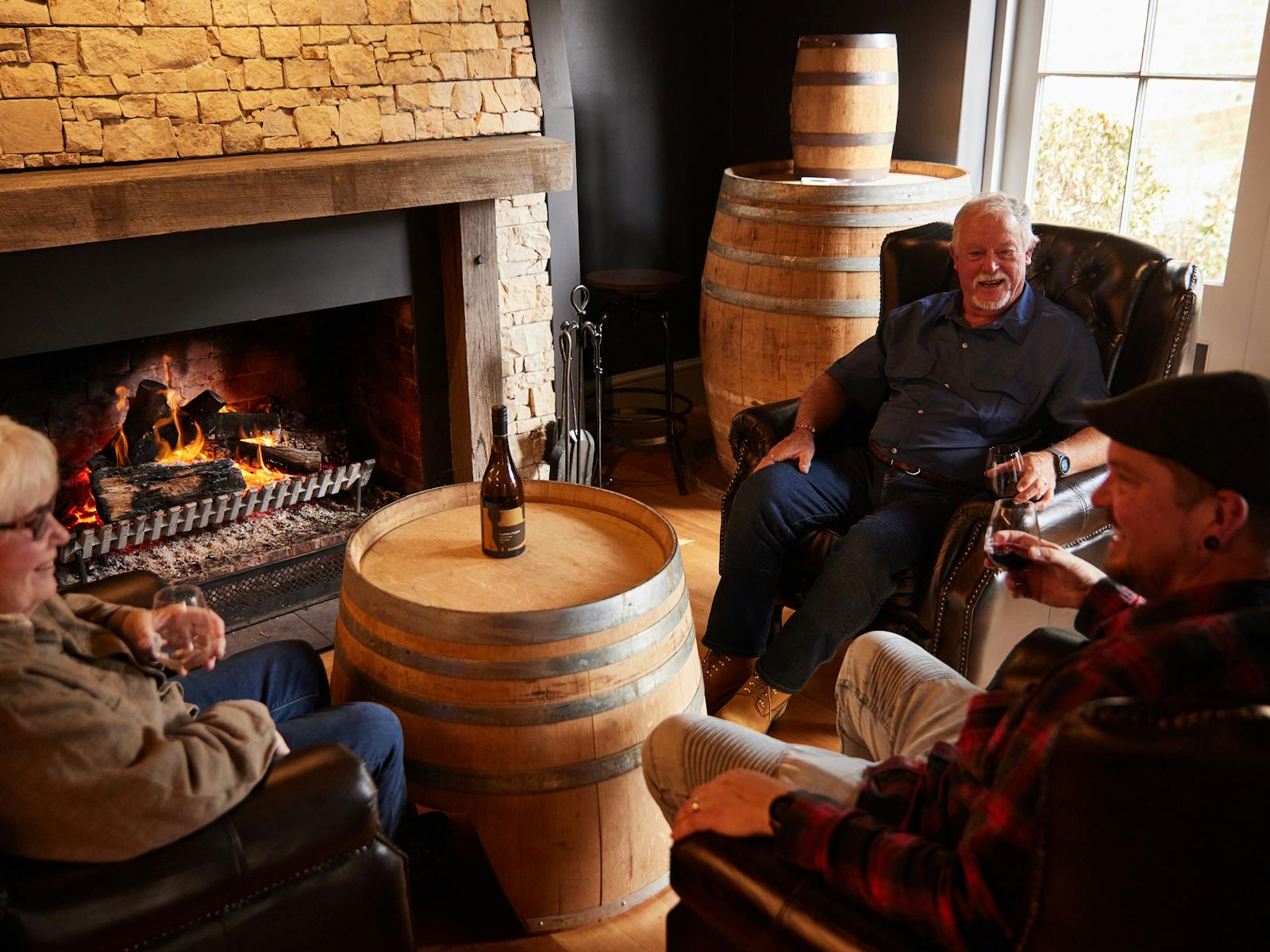 Three guests enjoying a drink in front of the  warm fireplace at Drink Tasmania Tasting House.