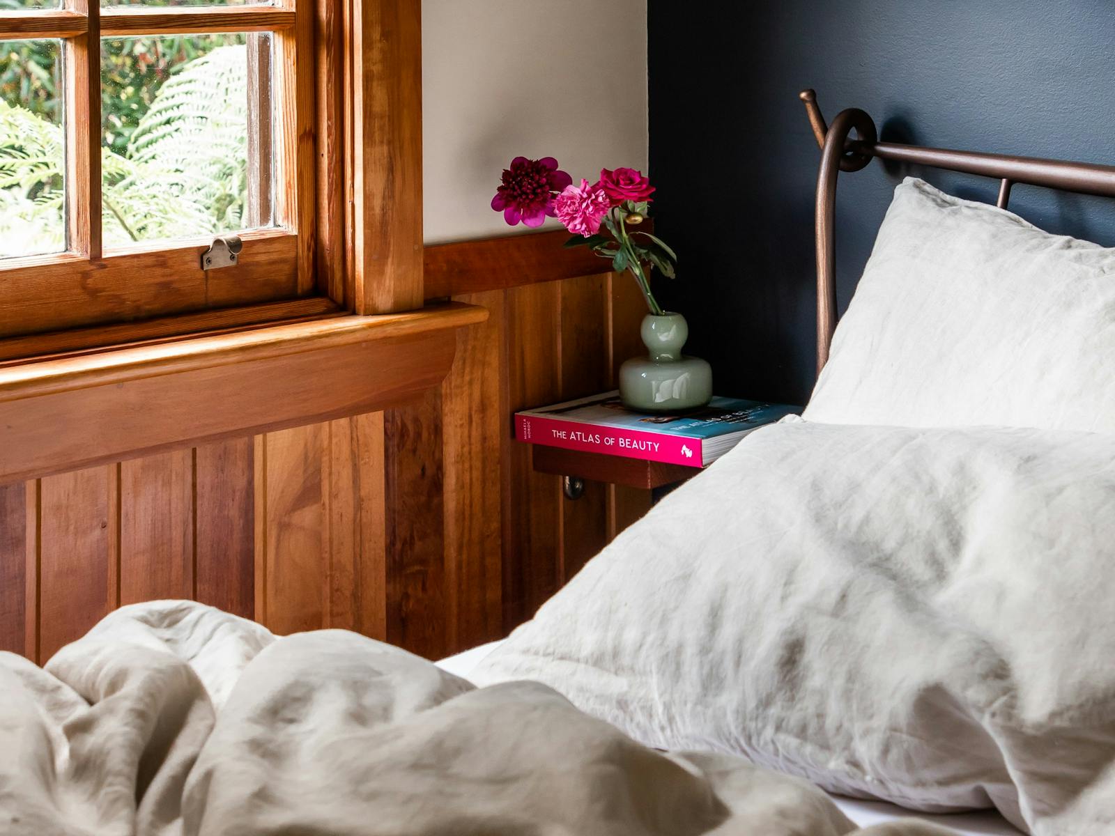 Corner of a bed with linen doona covers and pillow cases, there is a floating table