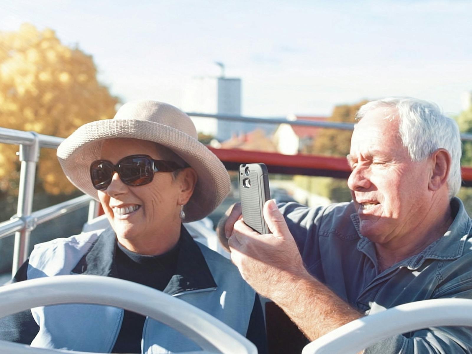 An older couple take photos of the sights from the  open-top double decker bus.