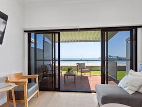View from living space including armchair, table, lounge, and outdoor timber deck, and view of beach