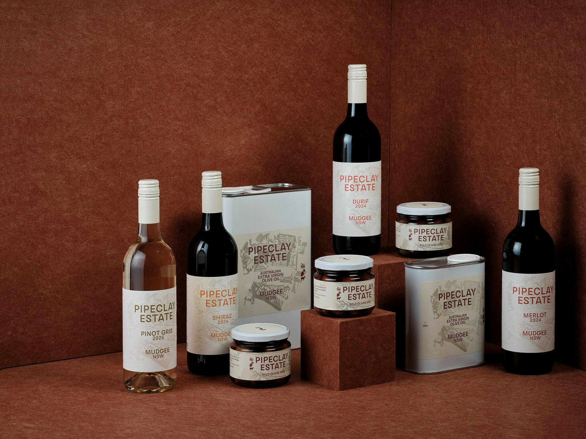 Lineup of Pipeclay Estate products including wines, olives and oil, set against terracotta backgdrop