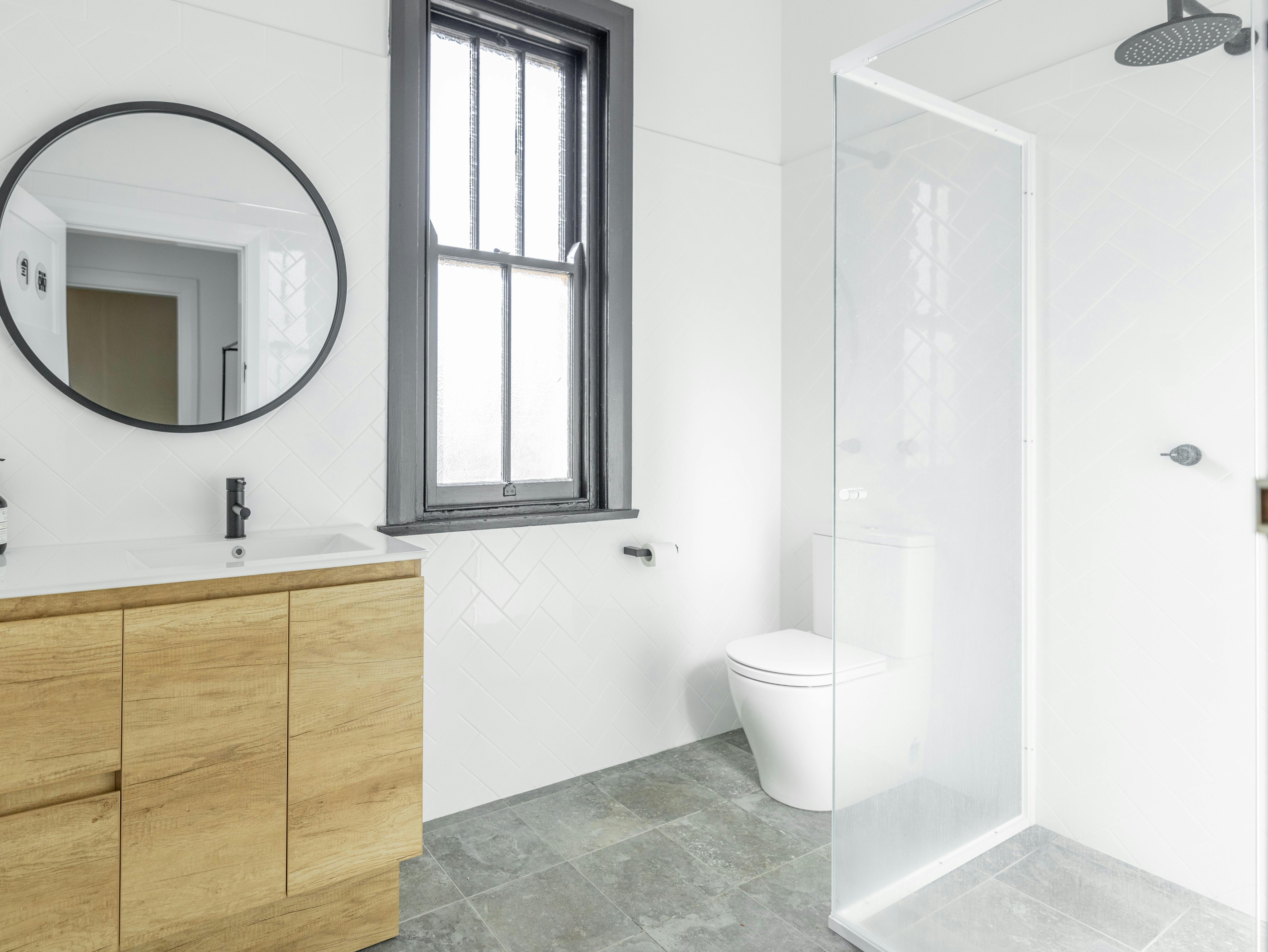 Bathroom with sink, mirror, toilet, window and shower.