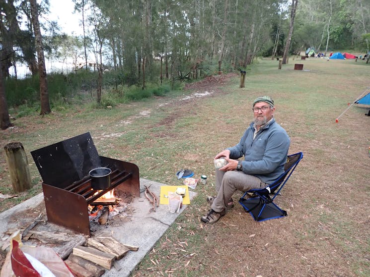 A person is siting beside a fire cooking lunch during the Myall Lakes paddling day