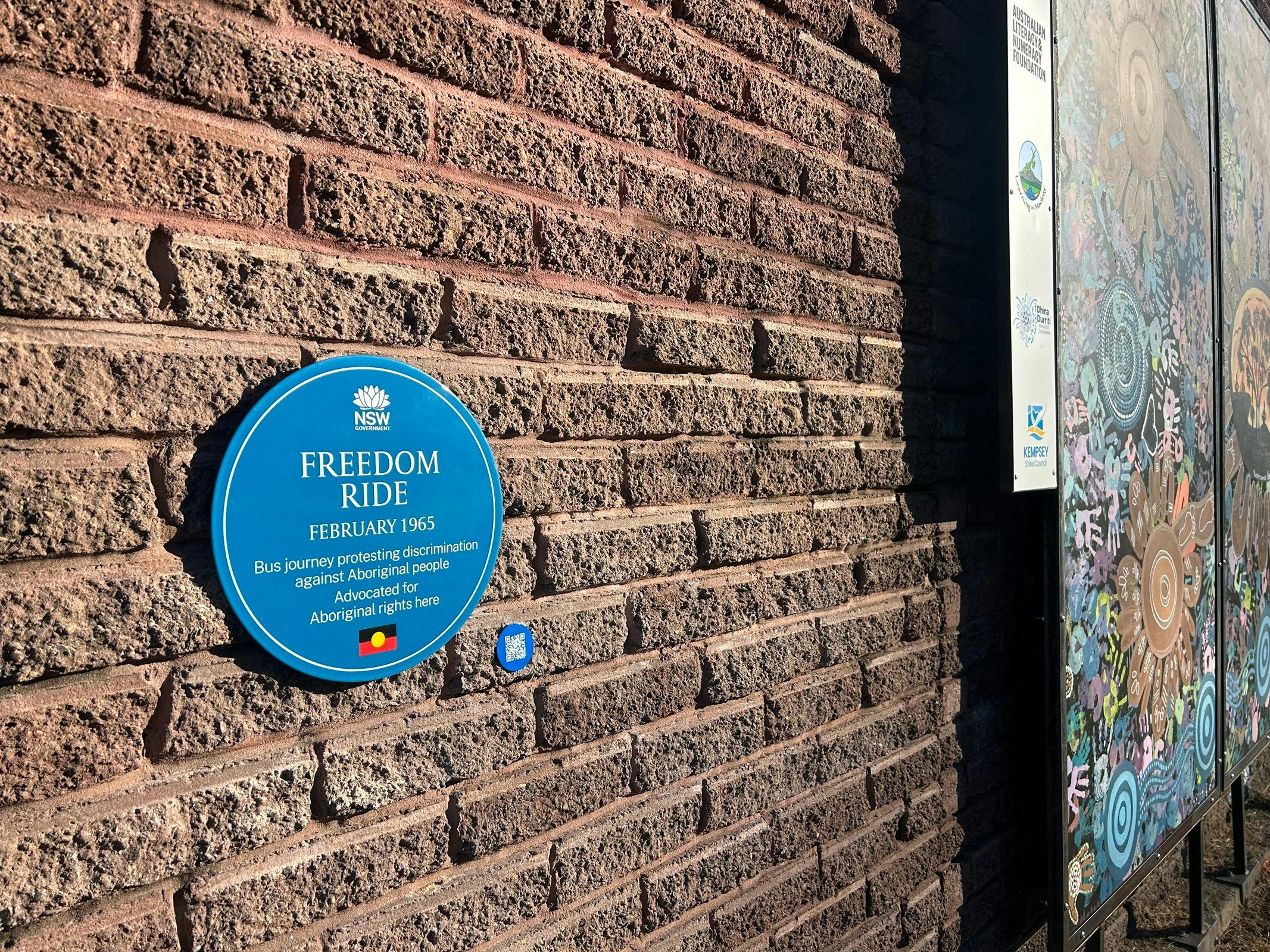 Blue plaque on textured brown brick wall next to art work
