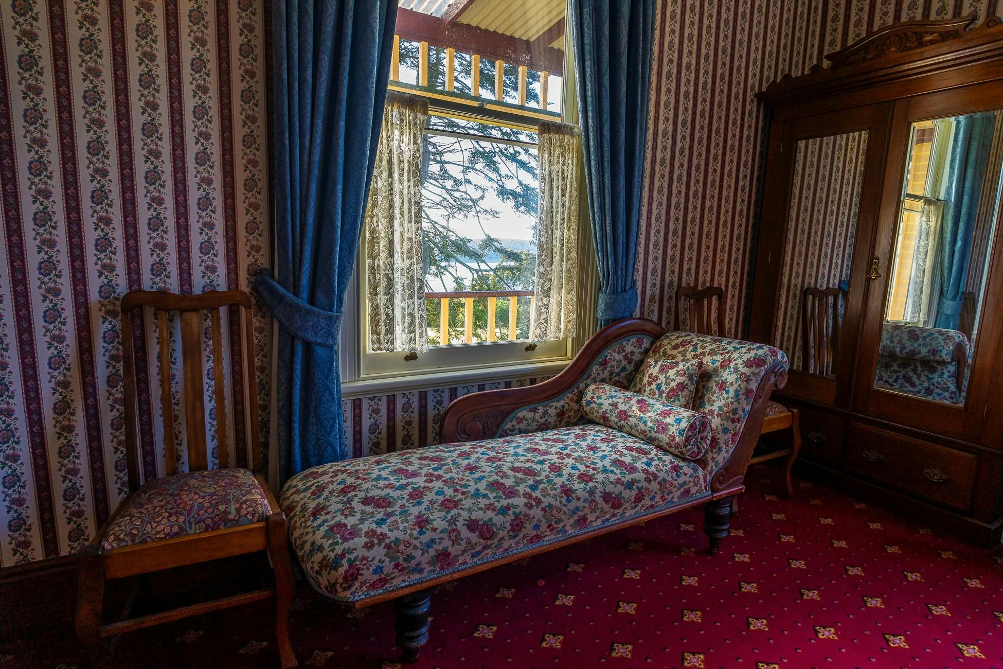 A patterned daybed in a heritage style home,  with a window looking out across beautiful gardens