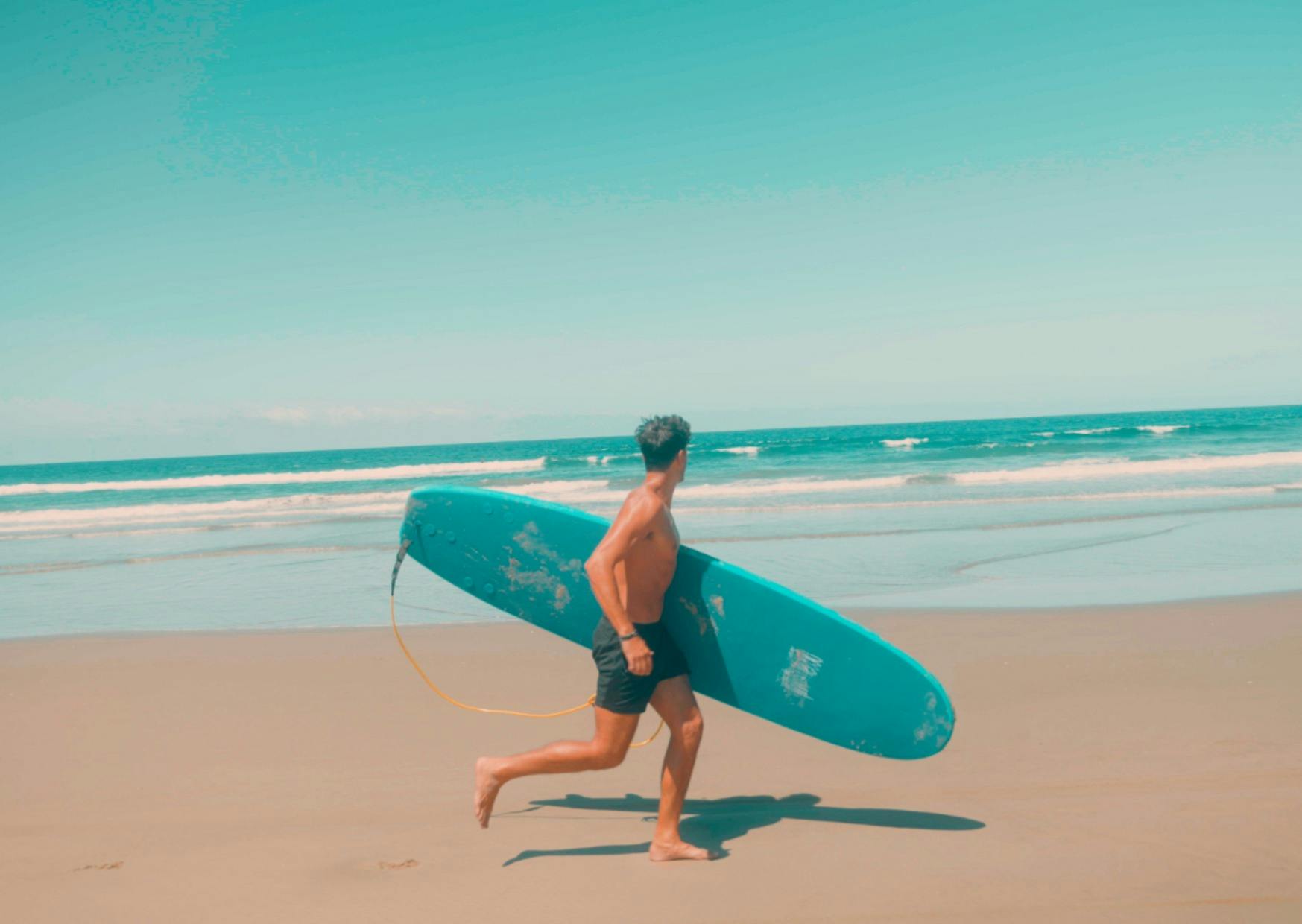 A man running on the beach with a surfboard in his hand.