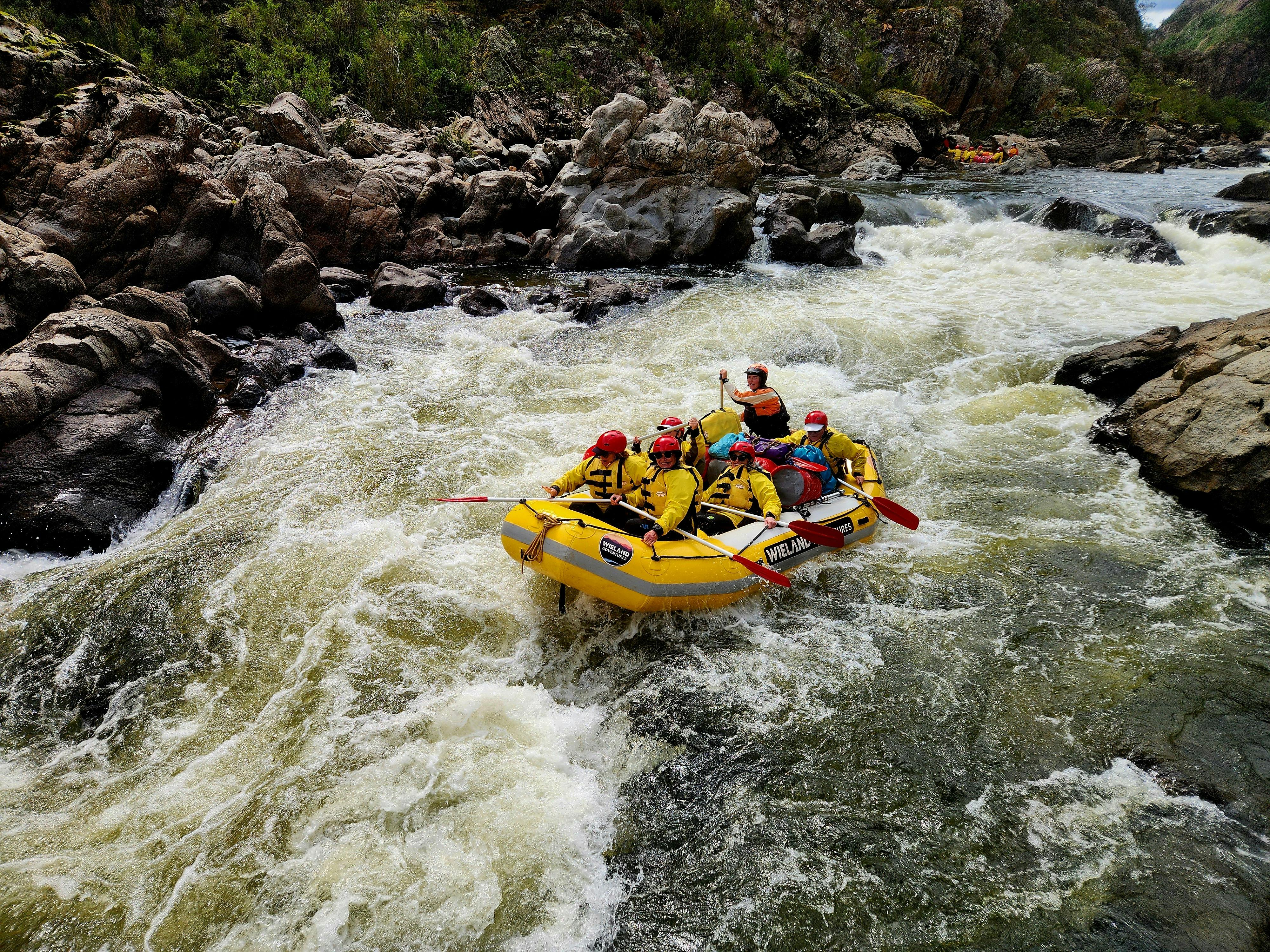A yellow whitewater raft on the Snowy River with a female raft guide and smiling clients in a rapid.