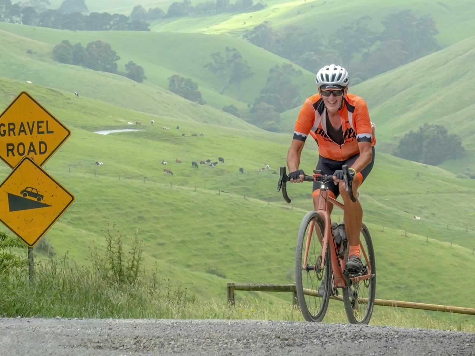Cyclist in orange jersey smiles as they reach the summit of the gravel track on Mt Misery