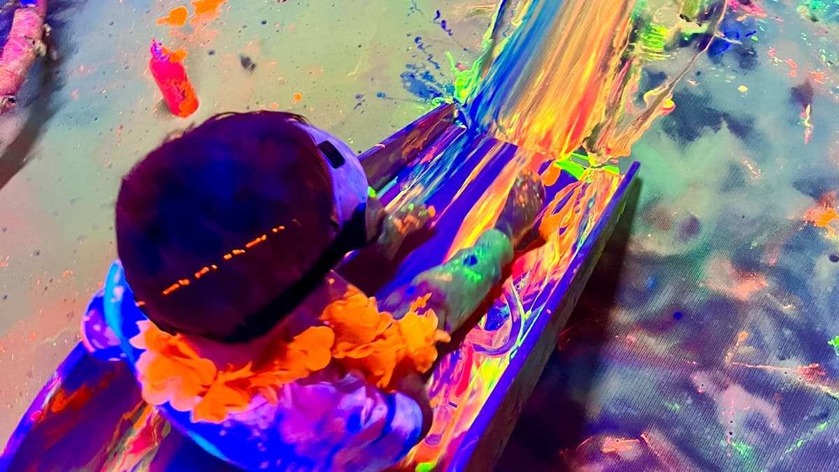 A boy sitting at the top of a slide that is covered in glowing paint at Messy Glow Co UV Paint Room