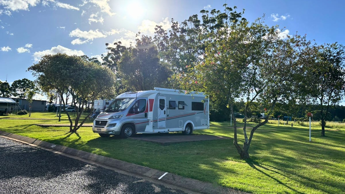 Motorhome parked on a spacious grassy powered site surrounded by trees at Yarraman Caravan Park.