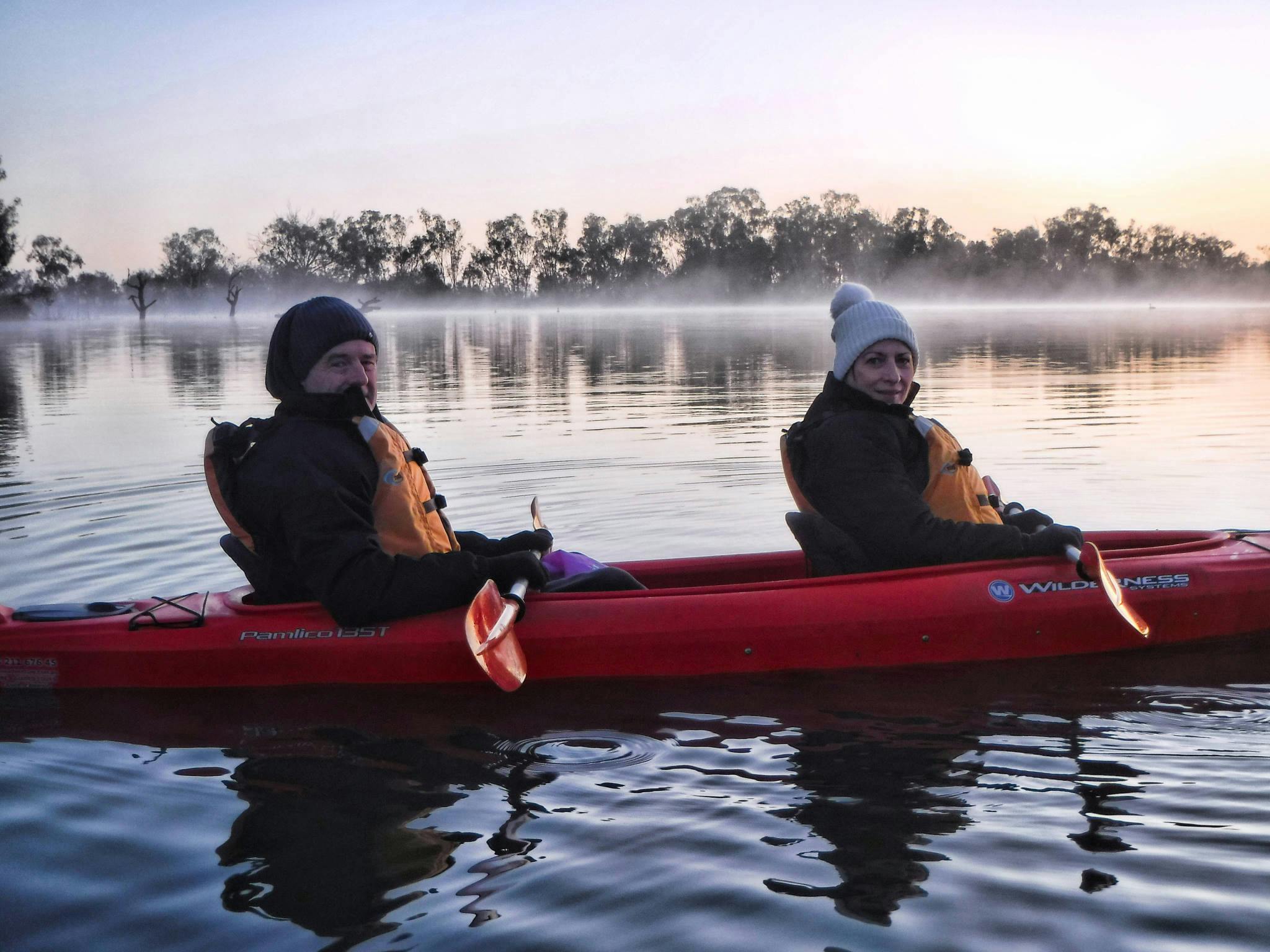 2 rugged-up kayakers in double kayak at sunrise, with mist sitting on the water
