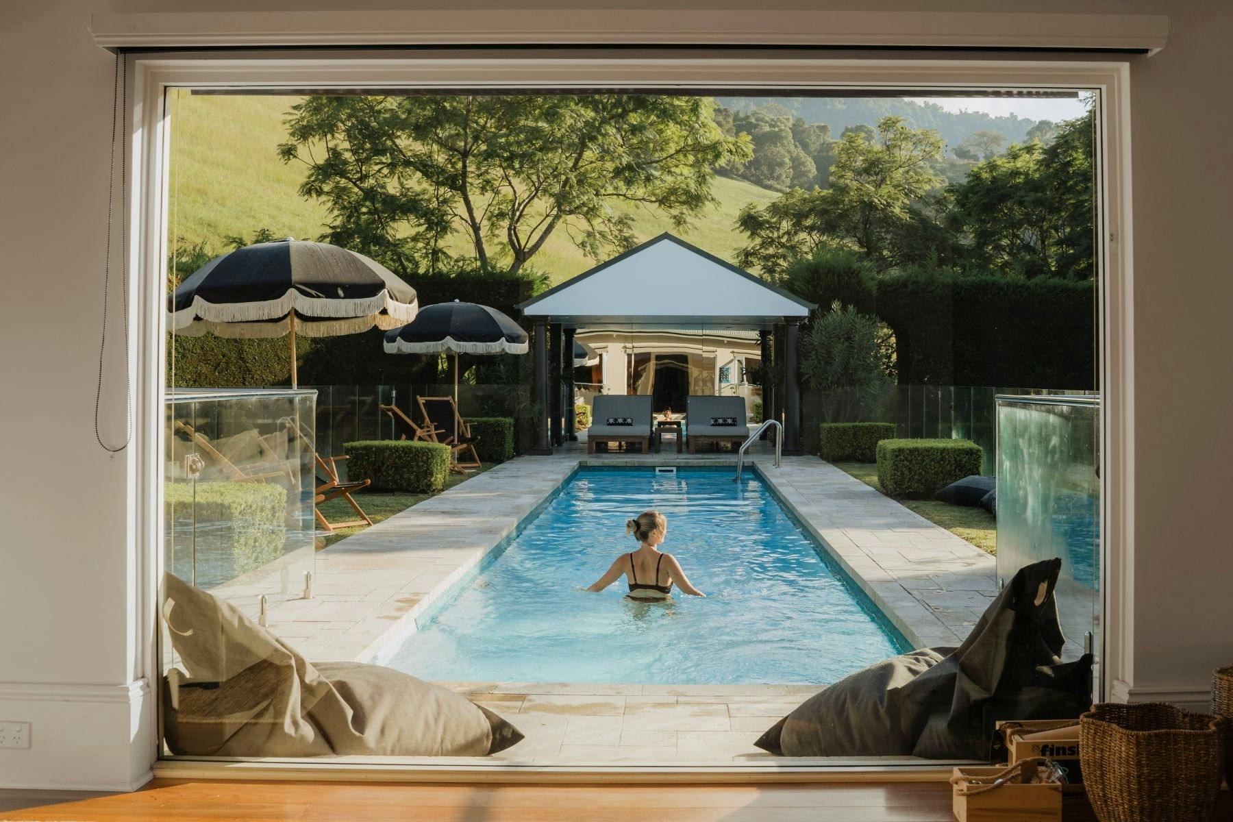 Image of pool area. Lady entering pool. two black unbrellas are open on the right hand side of  pool