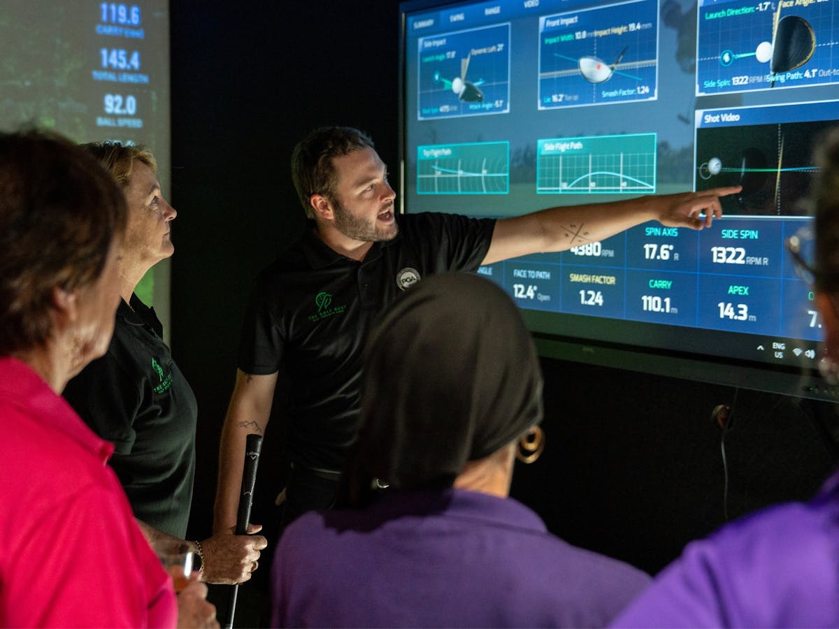 A male golf coach explains the data captured by the sim to a group of ladies