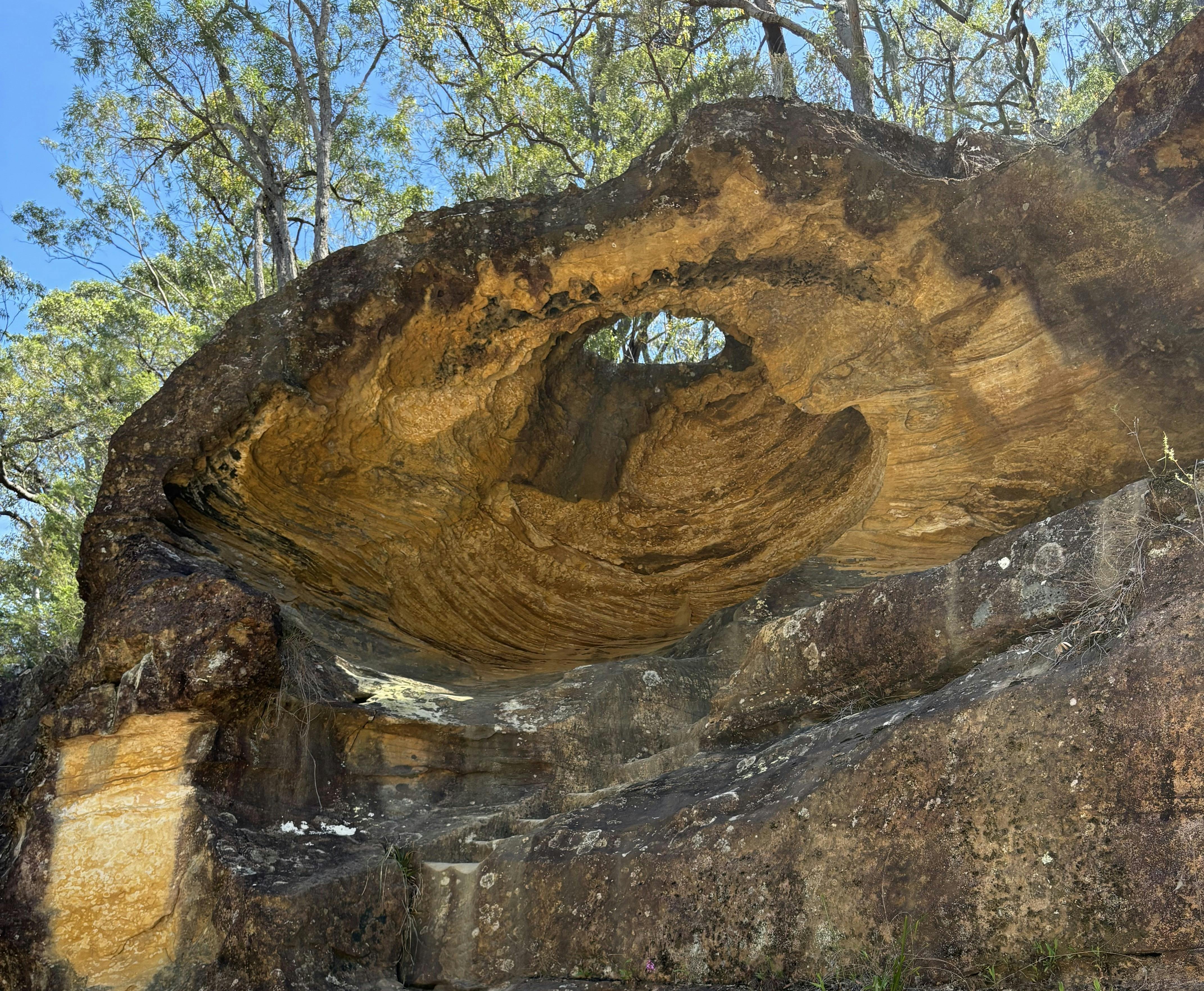 A sandstone cave with a hole in its roof silhouetted against the blue sky.