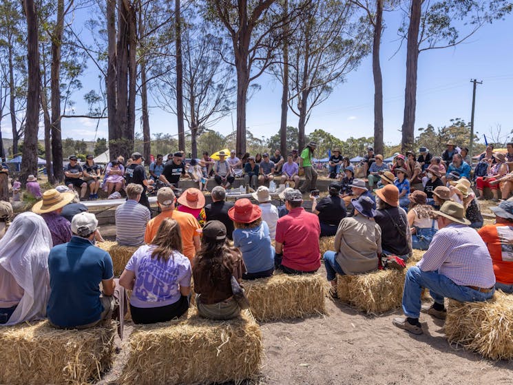 A chef presents a cooking class outdoors to crowds seated on straw bales at Giiyong Festival