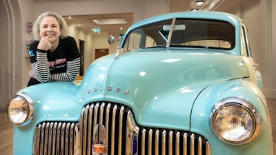 A woman poses on a vintage Holden car in an exhibition