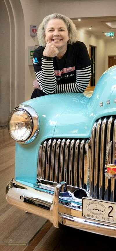 A woman poses on a vintage Holden car in an exhibition