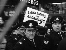 A black and white photo of police in front of a protest where banners say Land Rights for Aborigines