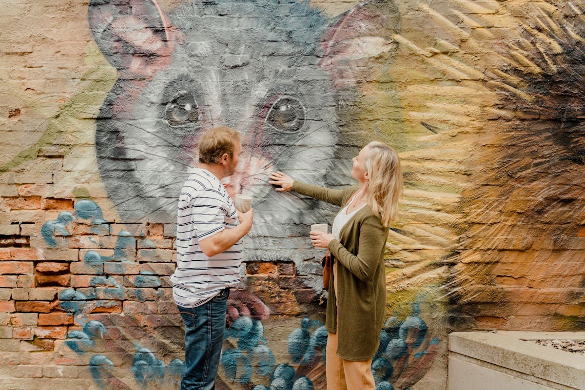 A man and woman touch a mural of a possum on a brick wall in Memorial Plaza, Corowa.