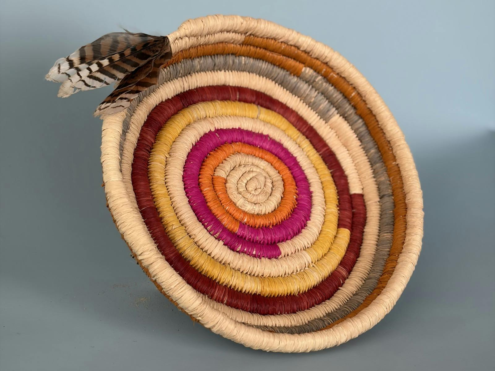 A colourful woven basket with feathers by a First Nations artist.