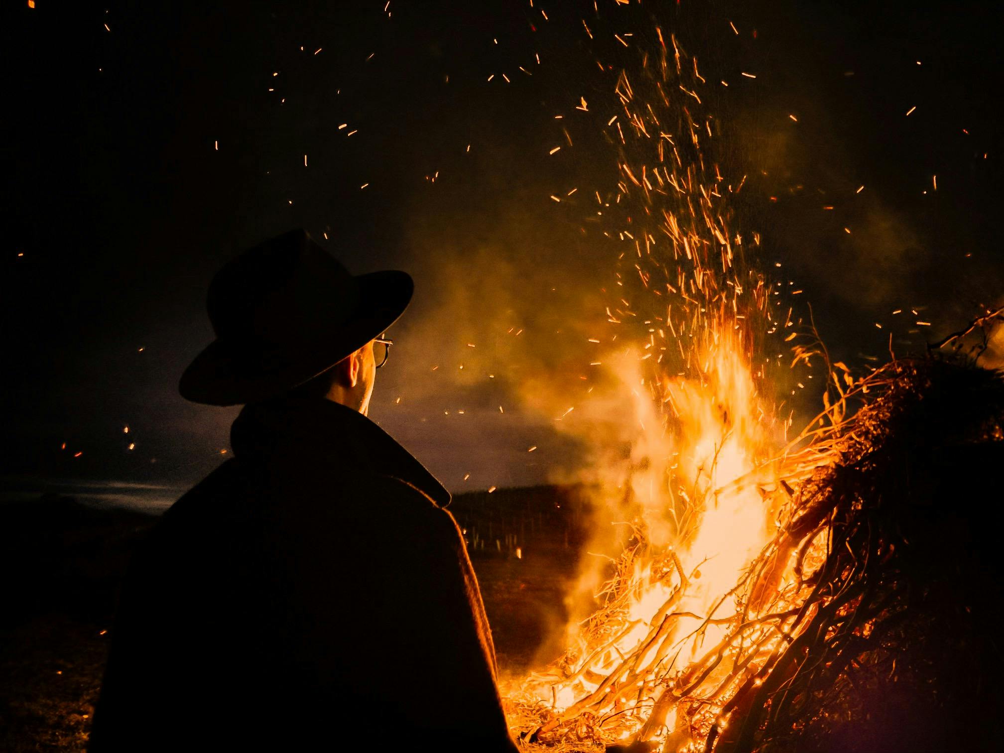 A man in a hat standing in front of a bonfire