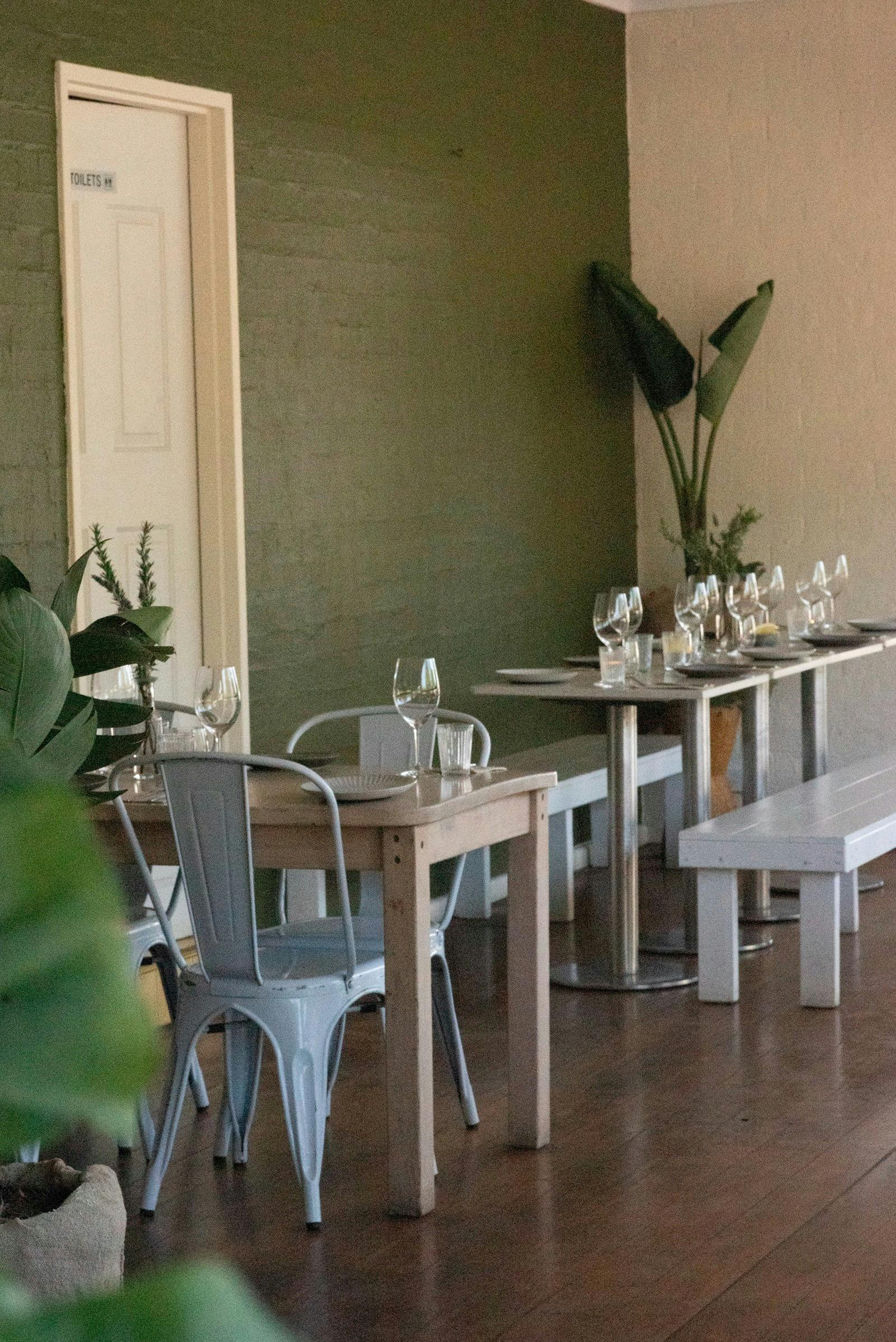 Elegant restaurant interior with wooden tables, stylish seating, greenery, and warm ambience.